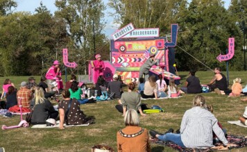 Outdoor theatre performance of Bin Rat, with people sat watching in the park