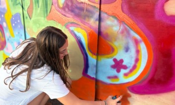 A girl adds orange spray paint to some street art.